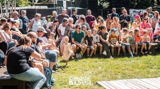 tribune met gezinnen met jonge kinderen, kijkend naar een podium in een groene omgeving